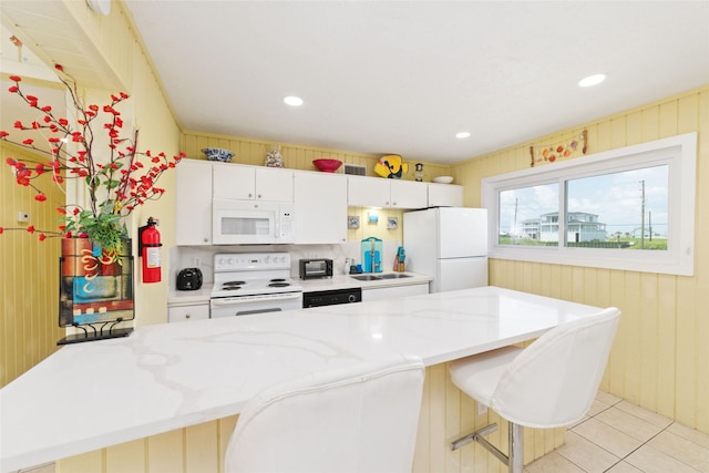 kitchen featuring white appliances, light tile patterned flooring, a sink, white cabinets, and a kitchen bar