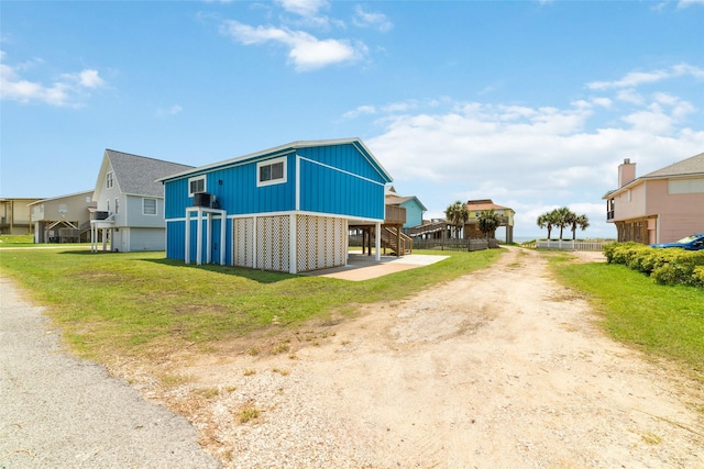 view of side of property with a lawn, dirt driveway, a residential view, a carport, and stairs