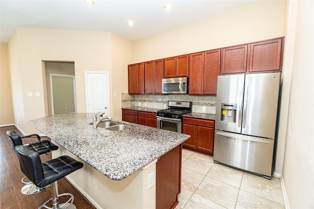 kitchen with a breakfast bar, an island with sink, a sink, backsplash, and appliances with stainless steel finishes