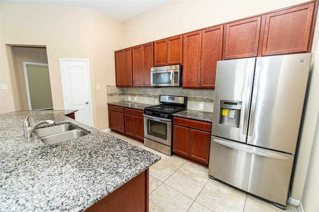 kitchen featuring dark stone countertops, light tile patterned floors, a sink, stainless steel appliances, and backsplash