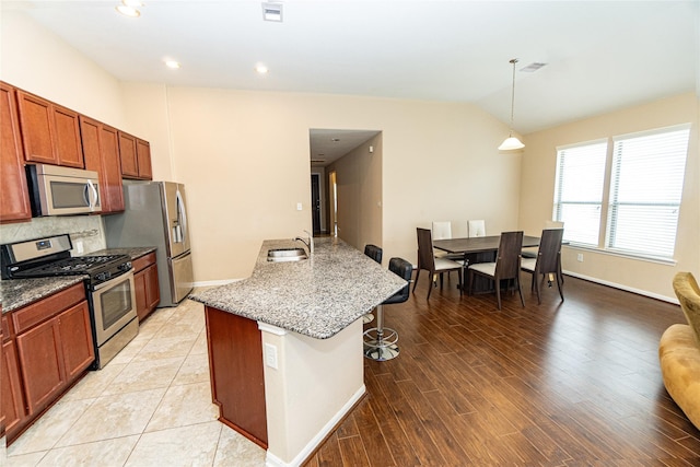 kitchen featuring a breakfast bar area, visible vents, lofted ceiling, stainless steel appliances, and decorative backsplash