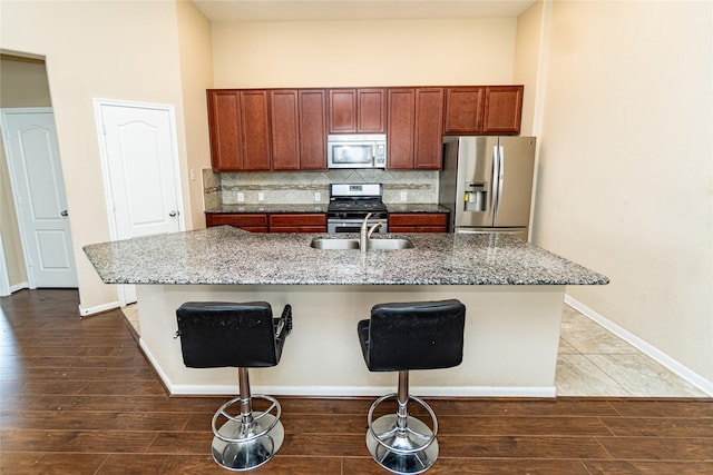 kitchen featuring a sink, tasteful backsplash, dark wood finished floors, appliances with stainless steel finishes, and a breakfast bar area