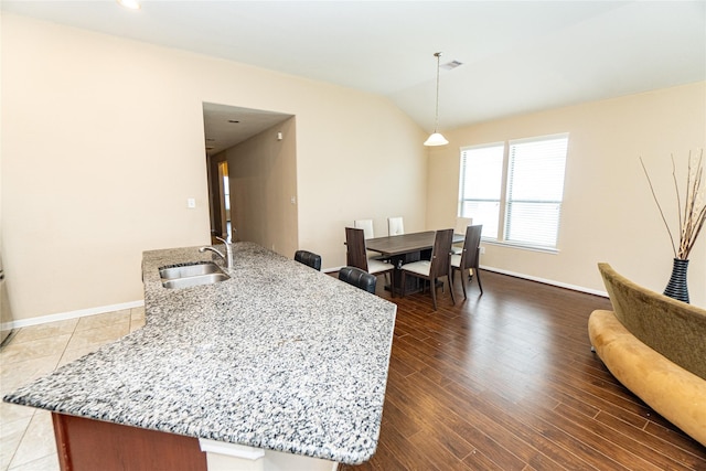 kitchen featuring visible vents, a sink, wood finished floors, lofted ceiling, and light stone countertops