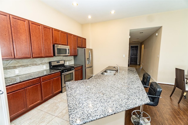 kitchen featuring light stone countertops, a sink, appliances with stainless steel finishes, a kitchen bar, and tasteful backsplash