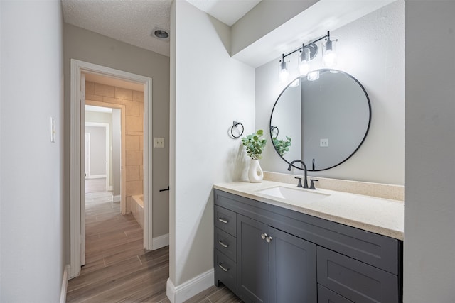 full bathroom with a washtub, a textured ceiling, wood finished floors, baseboards, and vanity