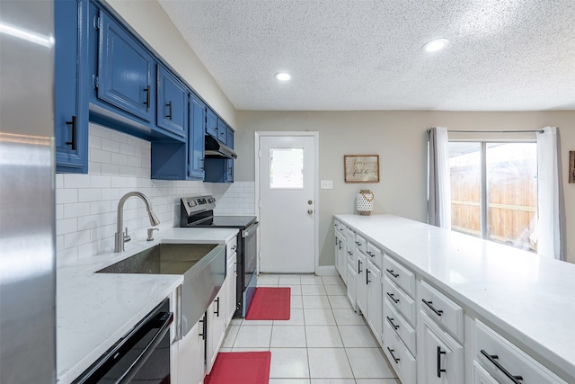 kitchen with blue cabinetry, under cabinet range hood, dishwasher, light tile patterned floors, and stainless steel electric range