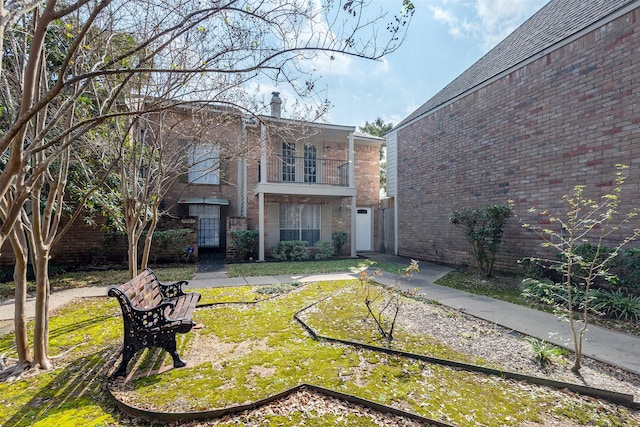 rear view of property featuring brick siding, a chimney, and a balcony