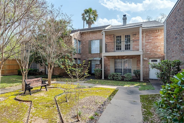 view of front of home featuring brick siding, fence, a front yard, a chimney, and a balcony