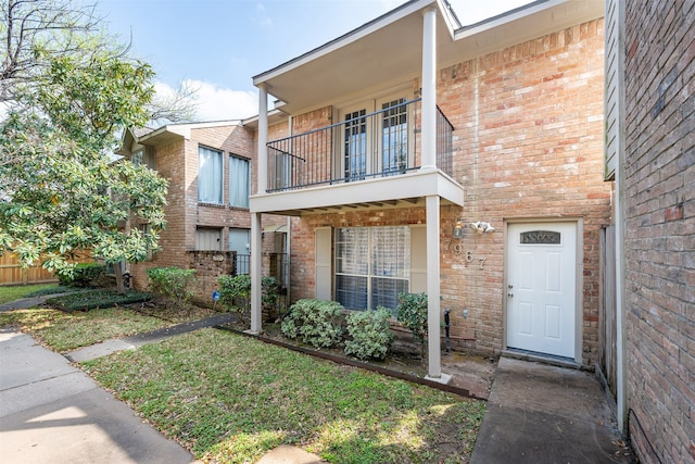 view of front of property with brick siding, a balcony, and fence