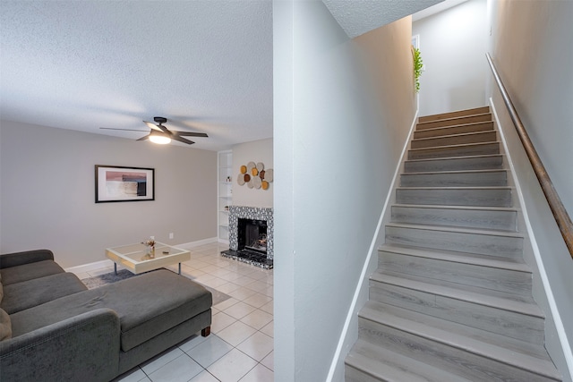 staircase with tile patterned floors, a textured ceiling, baseboards, ceiling fan, and a tile fireplace