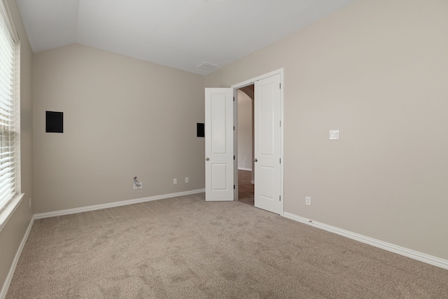 unfurnished bedroom featuring vaulted ceiling, multiple windows, carpet, and baseboards