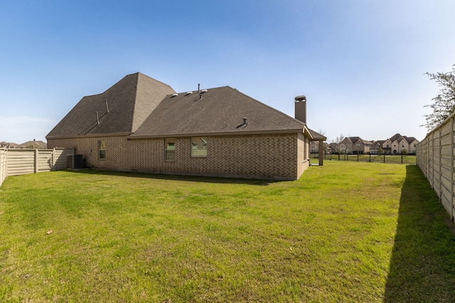 back of property with a fenced backyard, brick siding, and a yard