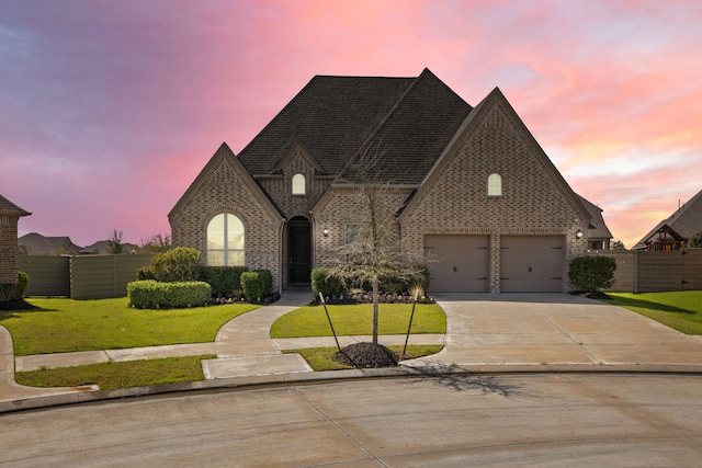 french country home featuring brick siding, fence, a garage, a yard, and driveway