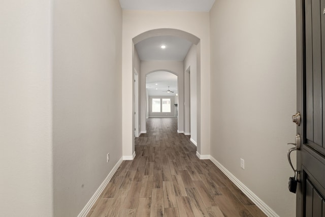 corridor with wood finished floors, arched walkways, and baseboards