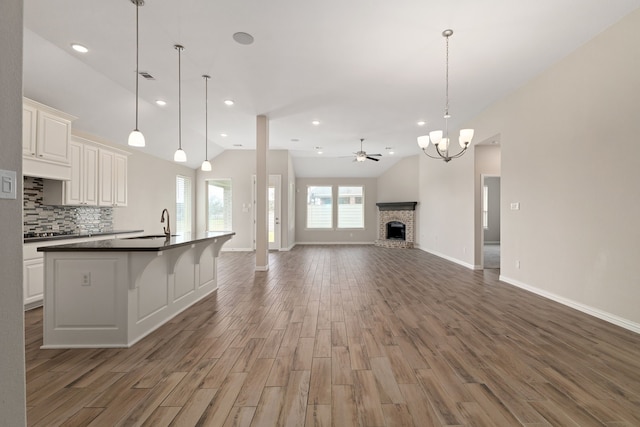 kitchen featuring wood finished floors, a fireplace, vaulted ceiling, dark countertops, and open floor plan