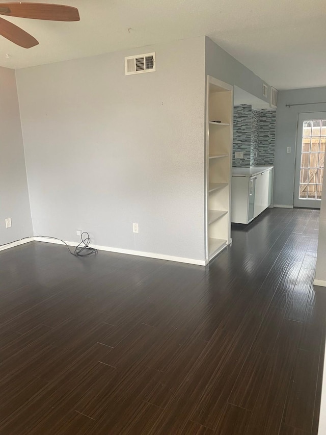 empty room with dark wood-style floors, visible vents, baseboards, and ceiling fan