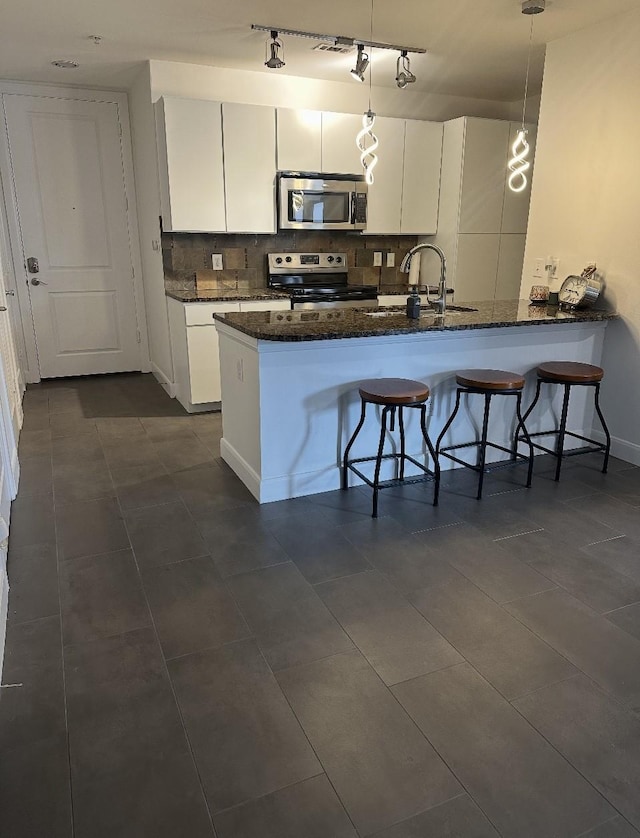 kitchen featuring a kitchen bar, a sink, dark stone counters, appliances with stainless steel finishes, and white cabinets