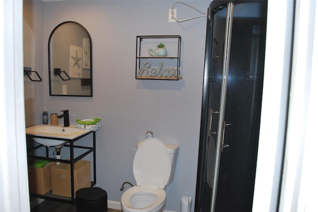 bathroom with toilet, a shower with door, and a sink