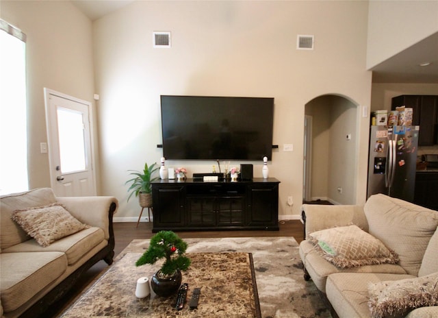 living area with wood finished floors, visible vents, arched walkways, and high vaulted ceiling