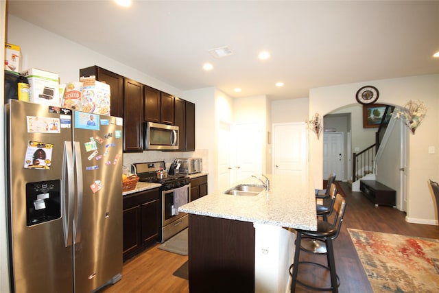 kitchen with a sink, stainless steel appliances, arched walkways, and dark wood-type flooring