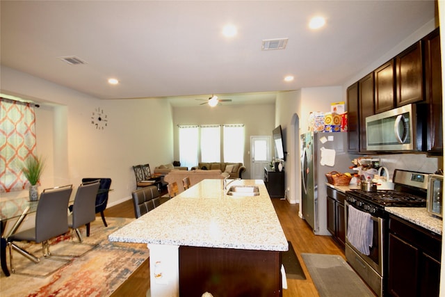 kitchen with a center island with sink, visible vents, arched walkways, a sink, and appliances with stainless steel finishes