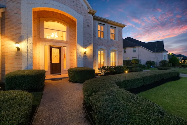 exterior entry at dusk with a yard and brick siding