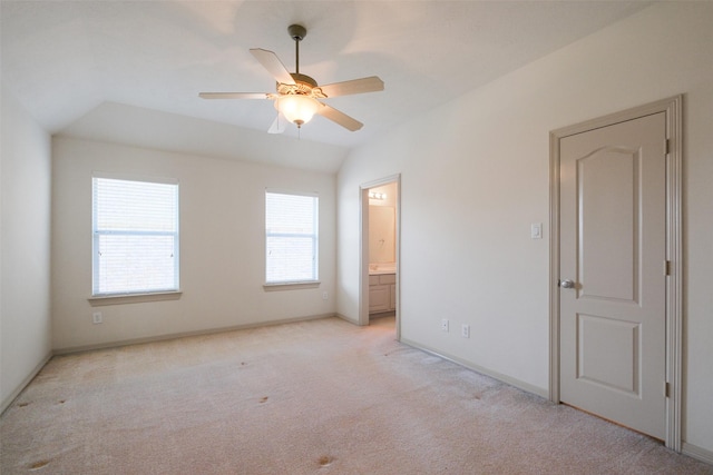 unfurnished bedroom with lofted ceiling, connected bathroom, baseboards, and light carpet