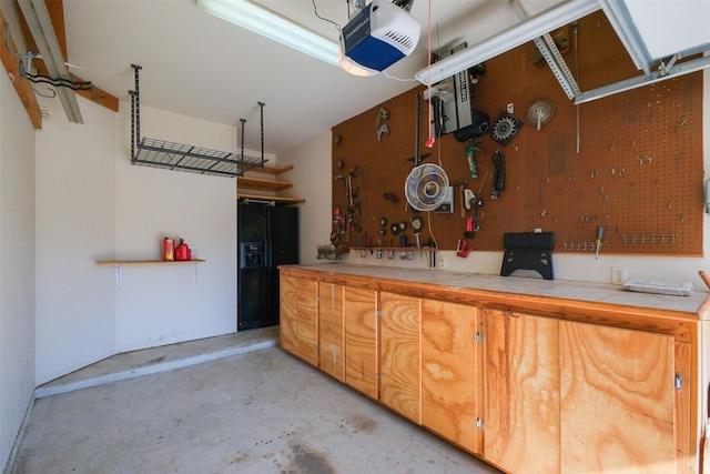 garage featuring a workshop area, a garage door opener, and black refrigerator with ice dispenser