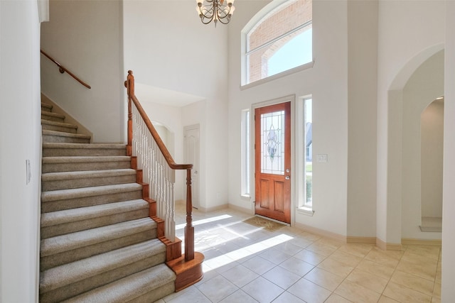 foyer entrance featuring light tile patterned floors, baseboards, a high ceiling, arched walkways, and stairs