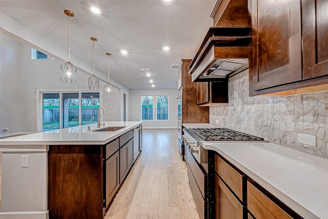 kitchen featuring light wood-style flooring, an island with sink, a sink, light countertops, and tasteful backsplash