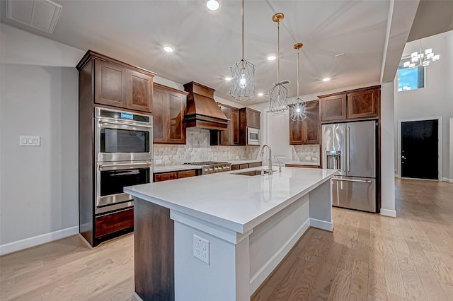 kitchen featuring visible vents, custom exhaust hood, a sink, stainless steel appliances, and light wood-type flooring