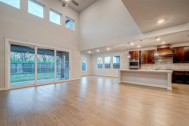 unfurnished living room with a sink, baseboards, light wood-style floors, and ceiling fan