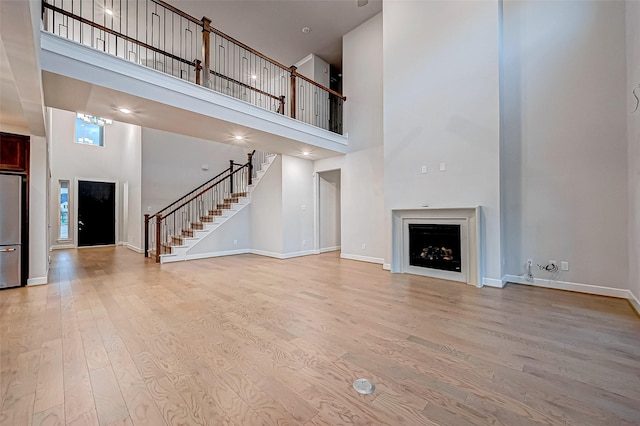 unfurnished living room with stairway, wood finished floors, baseboards, a high ceiling, and a fireplace