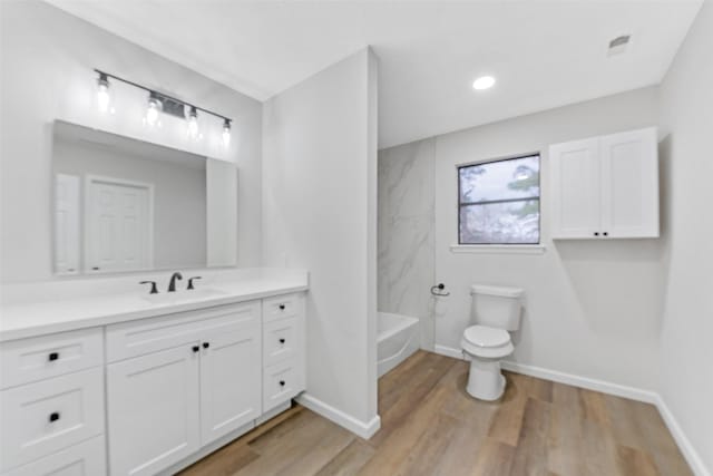 full bathroom with baseboards, toilet, a tub to relax in, wood finished floors, and vanity