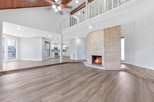 unfurnished living room featuring a fireplace, a high ceiling, baseboards, and wood finished floors