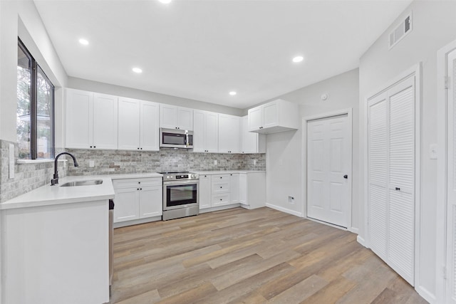 kitchen featuring visible vents, a sink, stainless steel appliances, light wood-style floors, and backsplash