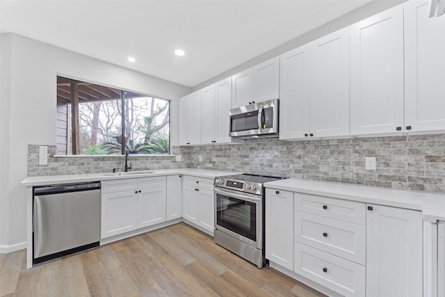 kitchen with a sink, stainless steel appliances, light wood-style floors, light countertops, and decorative backsplash