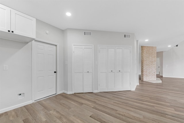 unfurnished bedroom with light wood-style floors, visible vents, and two closets