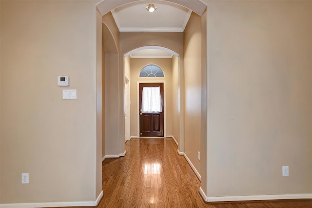 doorway to outside featuring wood finished floors, crown molding, baseboards, and arched walkways