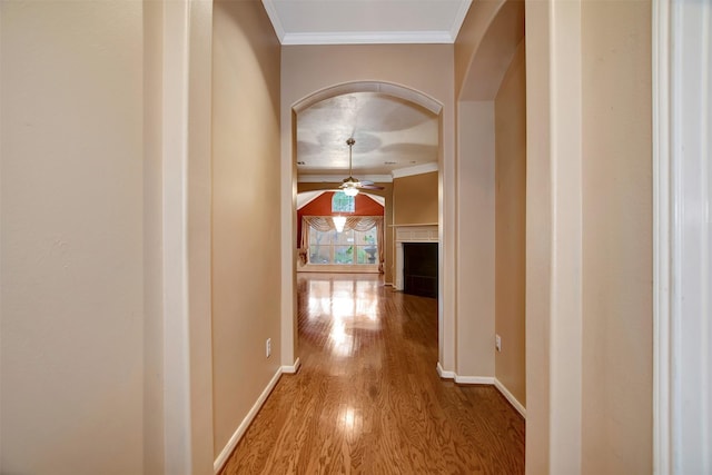 corridor featuring crown molding, wood finished floors, arched walkways, and baseboards