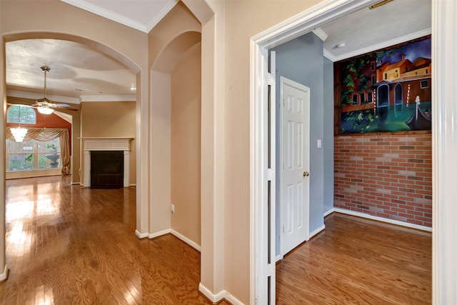 hall featuring baseboards, brick wall, wood finished floors, and crown molding