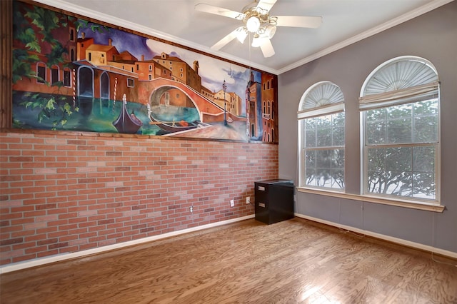 spare room with brick wall, crown molding, baseboards, ceiling fan, and wood finished floors