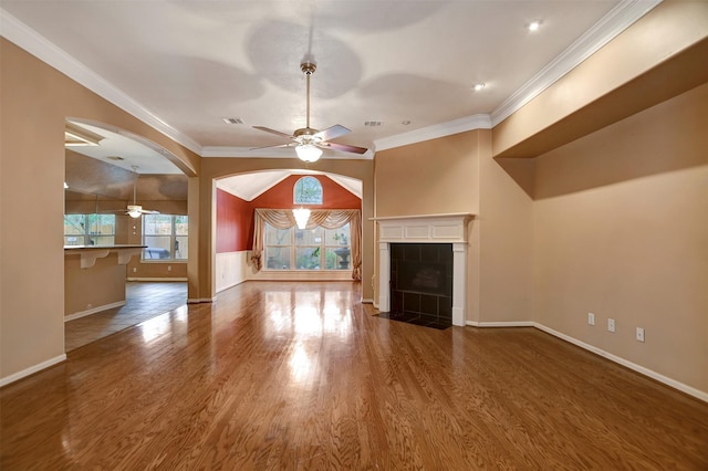 unfurnished living room featuring wood finished floors, baseboards, a tile fireplace, ceiling fan, and crown molding