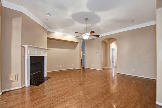 unfurnished living room with a ceiling fan, baseboards, wood finished floors, a fireplace, and arched walkways