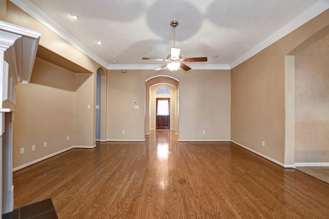 unfurnished living room with crown molding, baseboards, ceiling fan, wood finished floors, and arched walkways