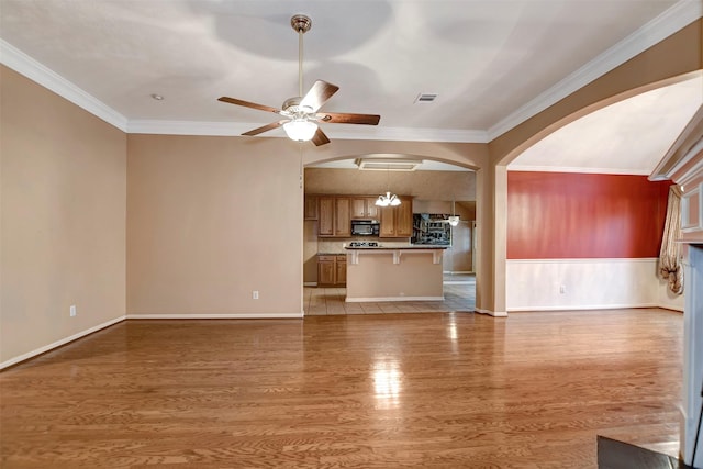 unfurnished living room with light wood finished floors, visible vents, ornamental molding, arched walkways, and a ceiling fan