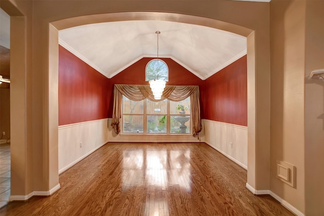 unfurnished room with lofted ceiling, ornamental molding, wainscoting, wood finished floors, and a notable chandelier