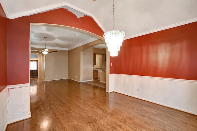 unfurnished room with crown molding, vaulted ceiling, ceiling fan with notable chandelier, wood finished floors, and arched walkways