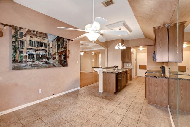 kitchen featuring visible vents, ceiling fan with notable chandelier, a sink, dark stone countertops, and vaulted ceiling