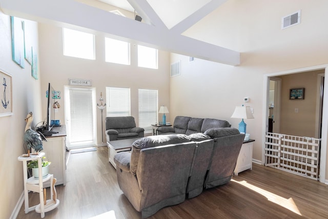 living area with a high ceiling, wood finished floors, visible vents, and baseboards